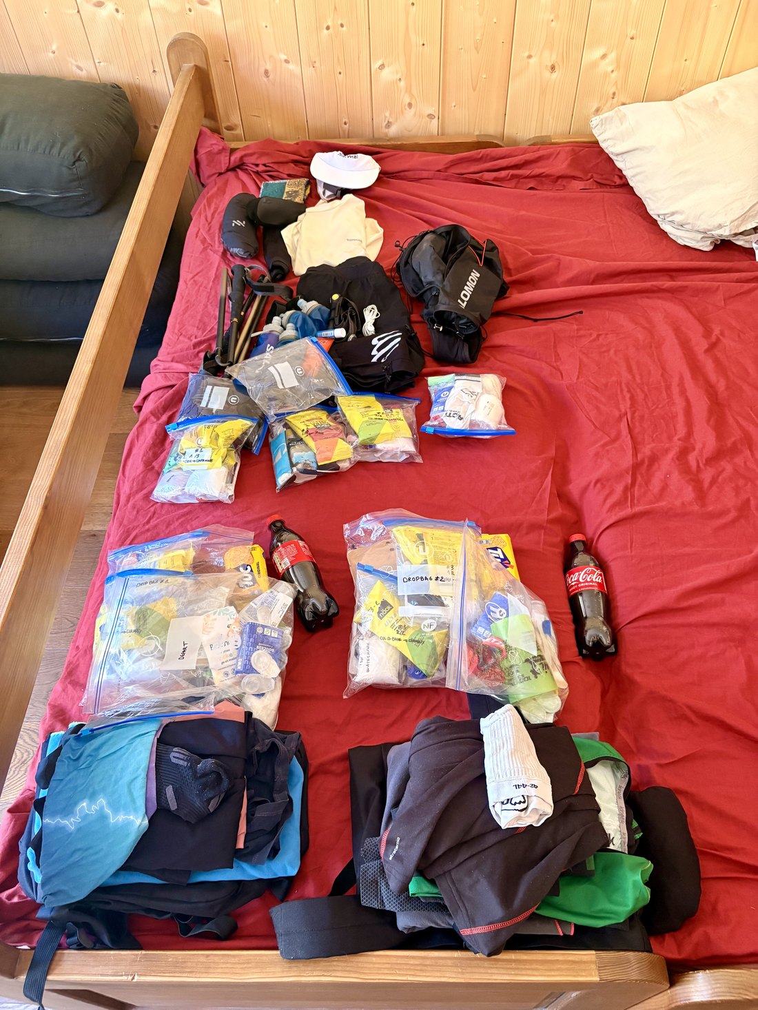 Tout le matériel de course étalé sur le lit : sacs de délestage, ziplocs de ravitaillement, vêtements, bâtons, bouteilles de Coca